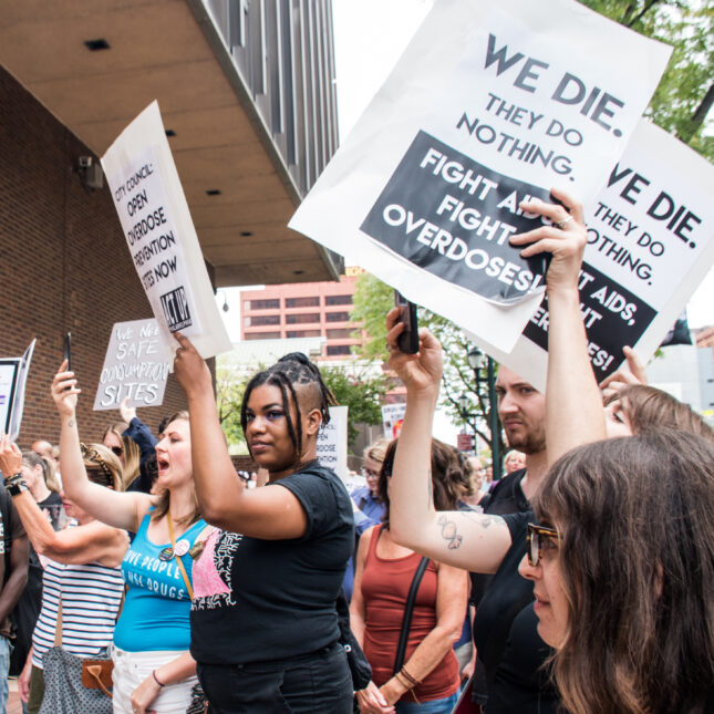 rally attendees raise up sign that advocate for safe consumption and overdose prevention sites in Philadelphia – coverage from STAT