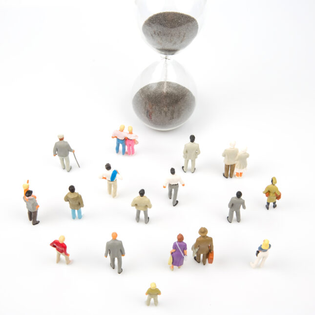 A crowd of miniature figurines facing towards an hourglass. -- cancer coverage from STAT