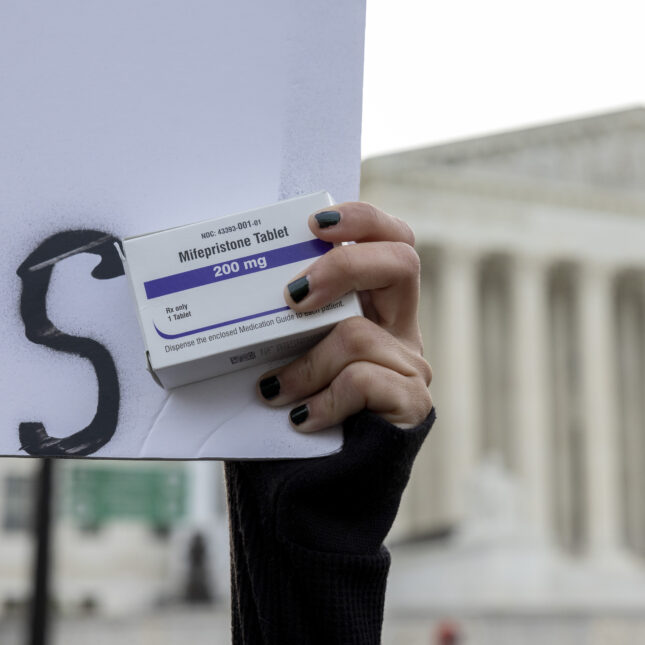 An abortion-rights activist raises a sign while holding a box of mifepristone pills in front of the Supreme Court — first opinion coverage from STAT