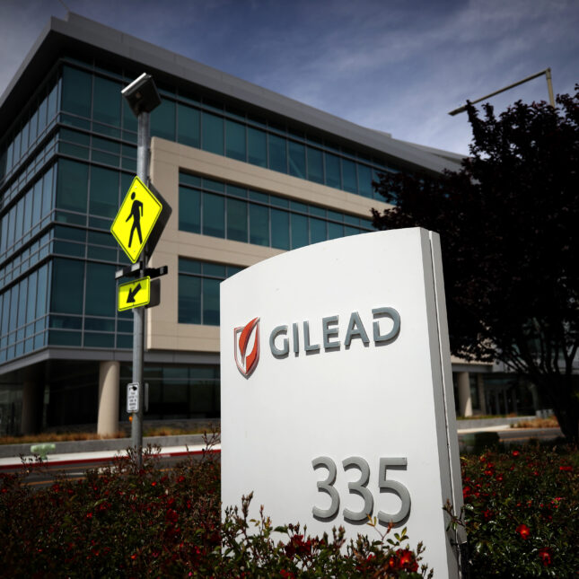 A sign of Gilead Sciences sits in front of its headquarter and next to a pedestrian crossing sign — health coverage from STAT