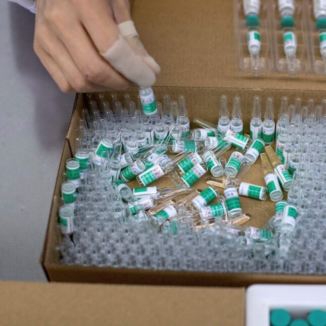 A person packages dozens of rabies vaccine in a box — coverage from STAT