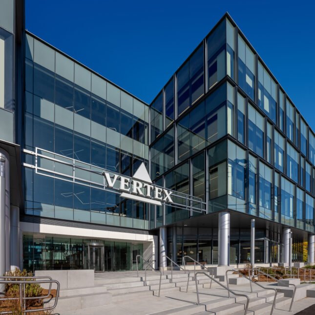 Stairs lead up to a glass building embellished with Vertex Pharmaceuticals' logo — coverage from STAT